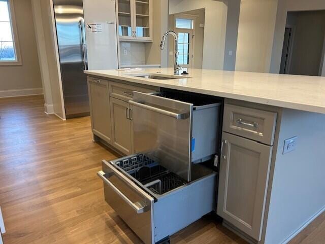 kitchen featuring high end refrigerator, light wood-type flooring, gray cabinets, and sink