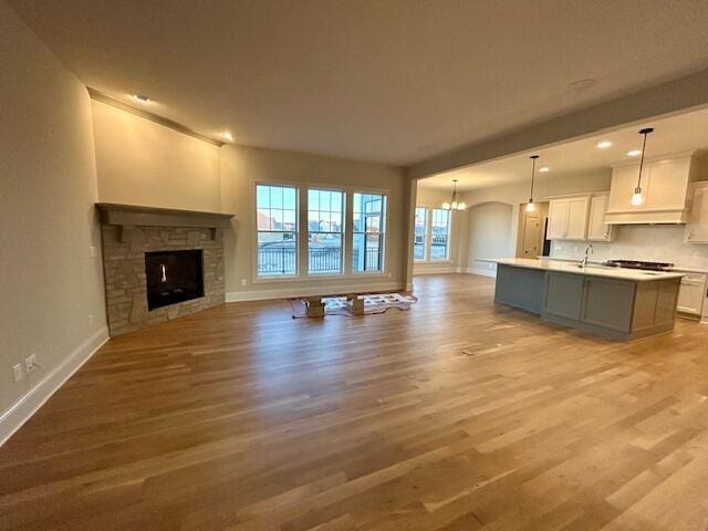 unfurnished living room with a fireplace, light hardwood / wood-style floors, a notable chandelier, and sink