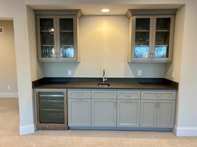 bar featuring light colored carpet, wine cooler, gray cabinetry, and sink