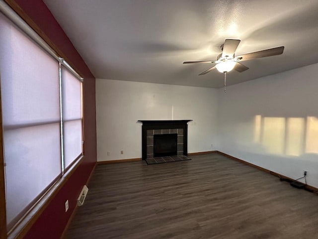 unfurnished living room featuring a tiled fireplace, dark hardwood / wood-style flooring, and ceiling fan