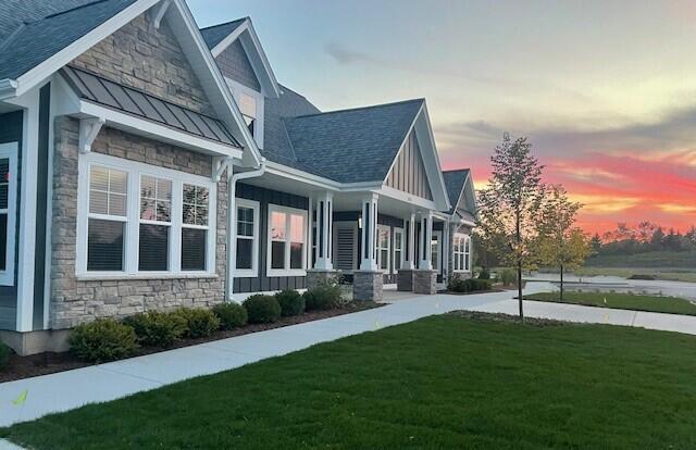 property exterior at dusk with covered porch and a lawn