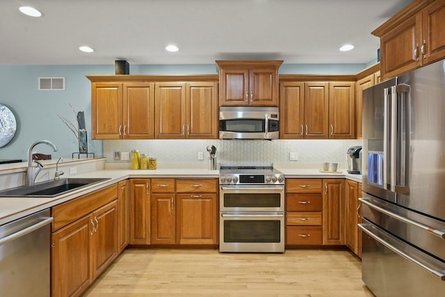 kitchen with appliances with stainless steel finishes, decorative backsplash, sink, and light wood-type flooring