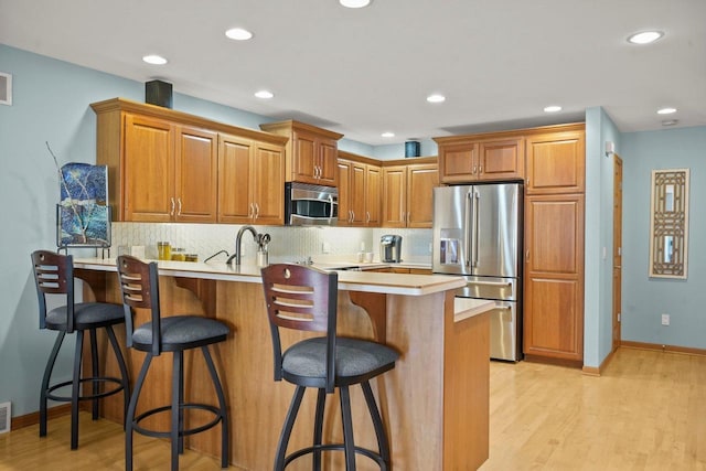 kitchen featuring kitchen peninsula, stainless steel appliances, backsplash, a breakfast bar, and light wood-type flooring