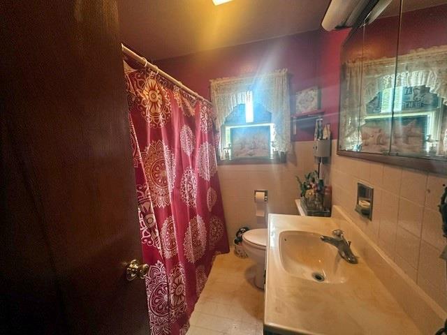 bathroom with vanity, tile patterned floors, walk in shower, tile walls, and toilet