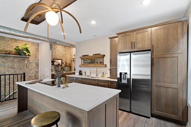 kitchen with sink, light hardwood / wood-style flooring, ceiling fan, brick wall, and stainless steel fridge