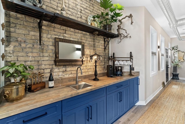 bar featuring blue cabinets, light hardwood / wood-style floors, brick wall, and sink