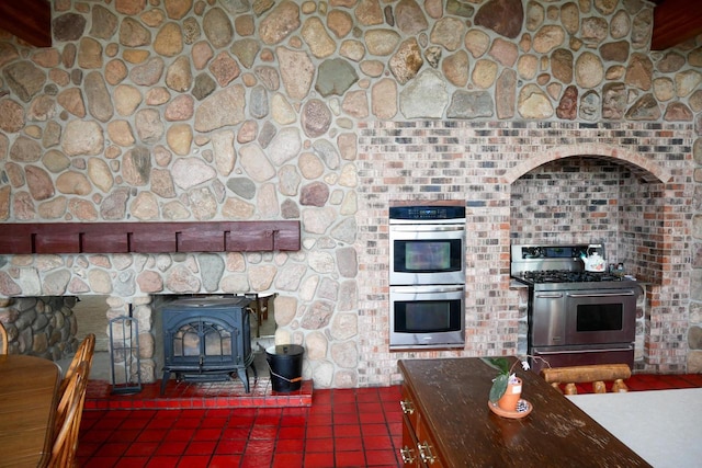 kitchen with appliances with stainless steel finishes, dark tile patterned floors, and a wood stove