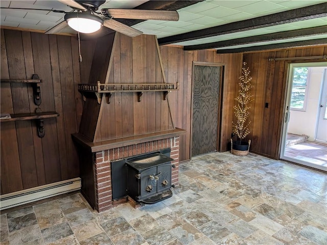 interior space featuring wood walls, a wood stove, beam ceiling, ceiling fan, and a baseboard radiator