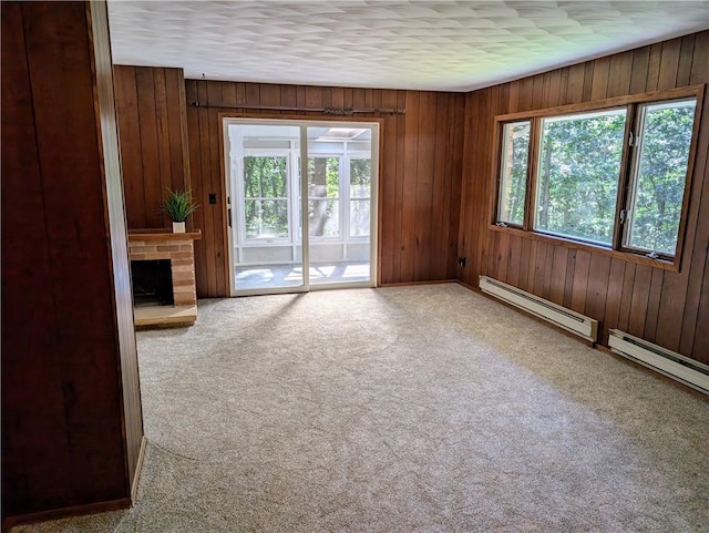 unfurnished living room with carpet, wood walls, a baseboard radiator, and a brick fireplace