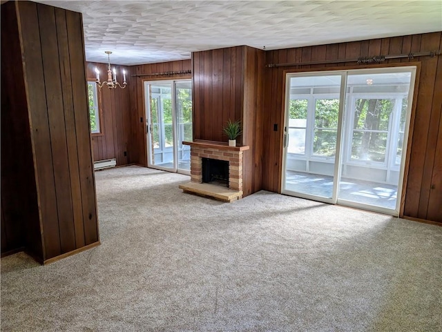 unfurnished living room with a brick fireplace, a chandelier, wood walls, and light colored carpet