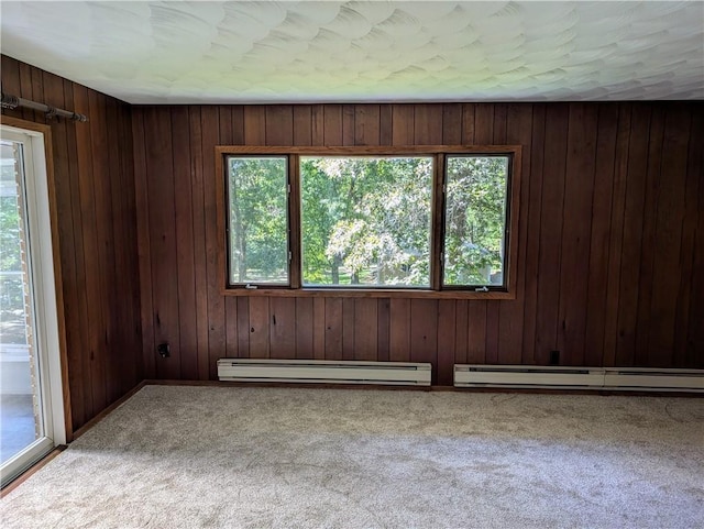 unfurnished room with wooden walls, a baseboard heating unit, and light colored carpet