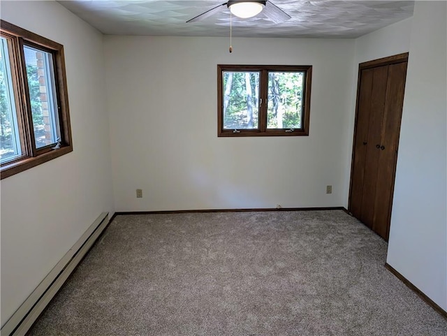 spare room featuring a healthy amount of sunlight, carpet flooring, ceiling fan, and a baseboard heating unit