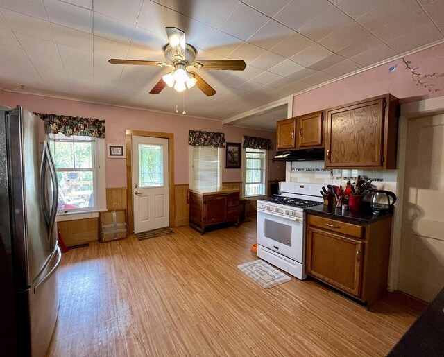 kitchen with light hardwood / wood-style floors, gas range gas stove, decorative backsplash, ceiling fan, and stainless steel fridge