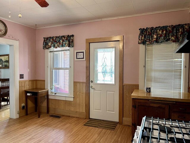 entryway with light wood-type flooring, crown molding, wooden walls, and ceiling fan