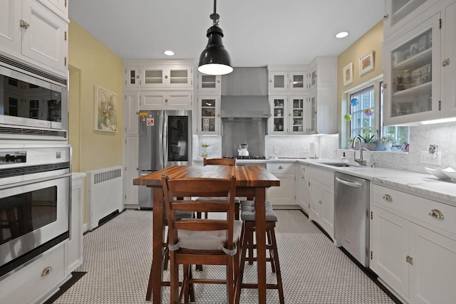 kitchen featuring pendant lighting, sink, radiator heating unit, wall chimney exhaust hood, and stainless steel appliances