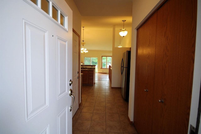 corridor with dark tile patterned flooring and an inviting chandelier