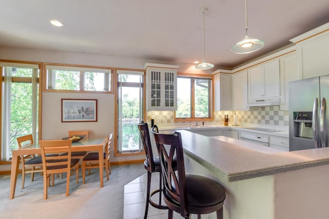 kitchen with hanging light fixtures, plenty of natural light, tasteful backsplash, and stainless steel fridge