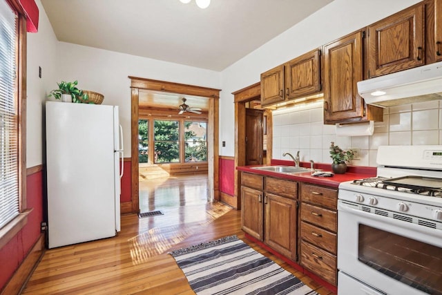 kitchen featuring light hardwood / wood-style floors, sink, decorative backsplash, white appliances, and ceiling fan