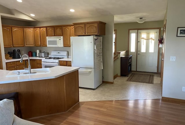 kitchen featuring vaulted ceiling, white appliances, kitchen peninsula, light wood-type flooring, and sink