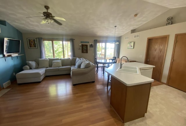 living room with light wood-type flooring, ceiling fan with notable chandelier, lofted ceiling, and sink