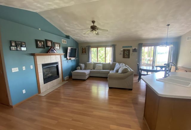 living room featuring light hardwood / wood-style floors, vaulted ceiling, a tile fireplace, ceiling fan with notable chandelier, and sink