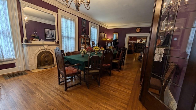 dining area featuring a fireplace, wood finished floors, visible vents, and crown molding