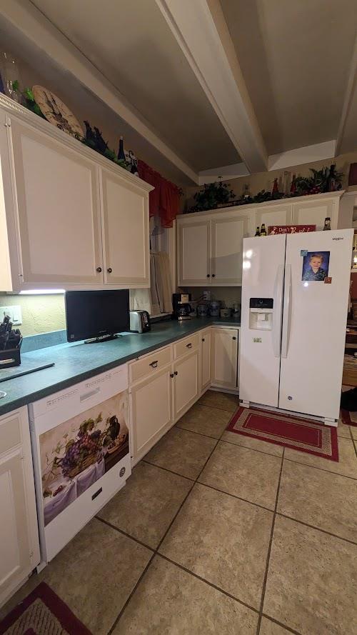 kitchen with light tile patterned floors, white fridge with ice dispenser, and white cabinetry