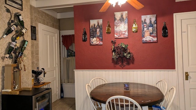 dining area featuring light tile patterned floors, visible vents, a ceiling fan, a textured wall, and a wainscoted wall