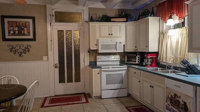 kitchen with white appliances, wainscoting, dark countertops, a sink, and light tile patterned flooring