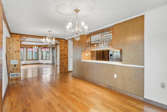 interior space featuring wood-type flooring, wooden walls, ornamental molding, and a notable chandelier