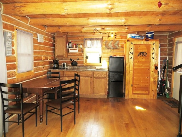 kitchen featuring beamed ceiling, light wood-type flooring, black refrigerator, and log walls