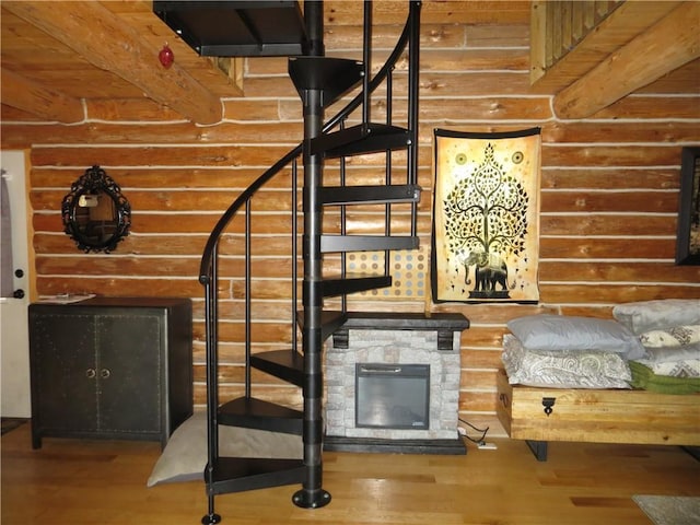 stairway featuring wood-type flooring, a fireplace, beam ceiling, and log walls