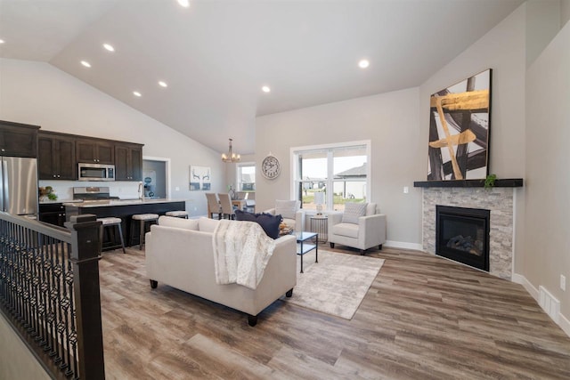 living room featuring light hardwood / wood-style floors, a fireplace, an inviting chandelier, and high vaulted ceiling