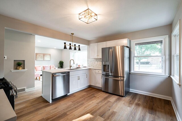 kitchen with pendant lighting, stainless steel appliances, kitchen peninsula, and white cabinetry