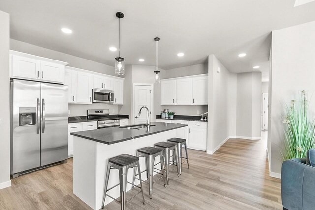 2876 Wild Goose Way, Stoughton, WI 53589 - kitchen featuring dark countertops, appliances with stainless steel finishes, a sink, light wood-style floors, and a breakfast bar area