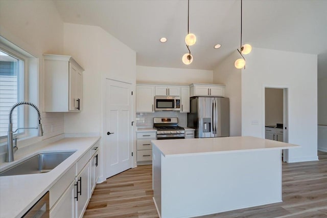 kitchen with a center island, white cabinets, sink, hanging light fixtures, and appliances with stainless steel finishes