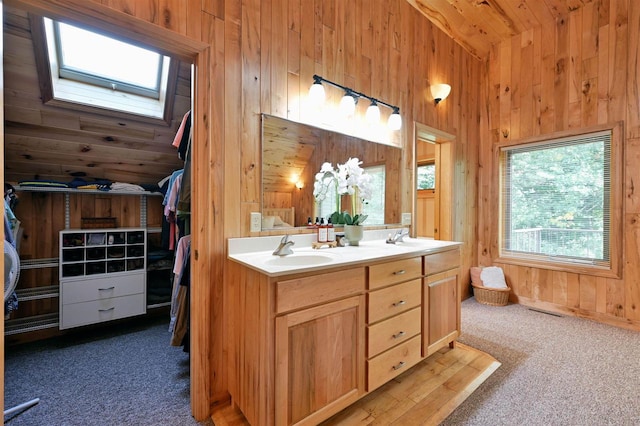 bathroom with vaulted ceiling with skylight, vanity, and wooden walls