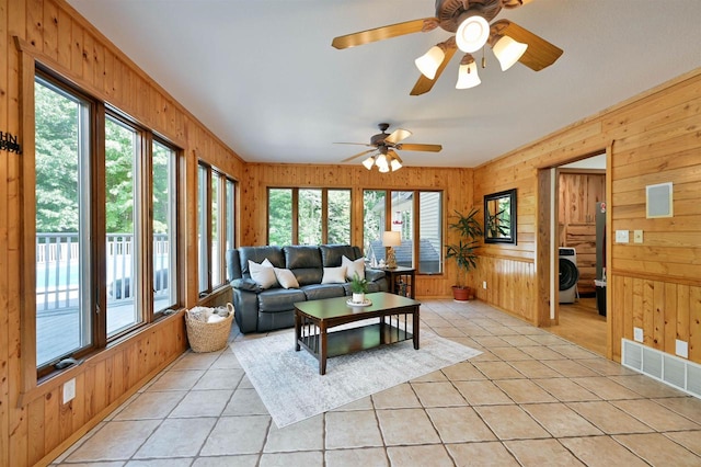 living room featuring washer / clothes dryer, wooden walls, ceiling fan, and a wealth of natural light