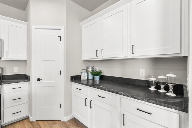 kitchen with white cabinetry, dark stone counters, and light wood finished floors