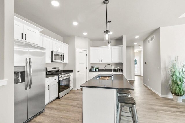 kitchen with light wood-style flooring, stainless steel appliances, dark countertops, white cabinetry, and a sink