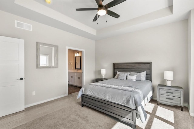 carpeted bedroom featuring visible vents, baseboards, a ceiling fan, a raised ceiling, and ensuite bath