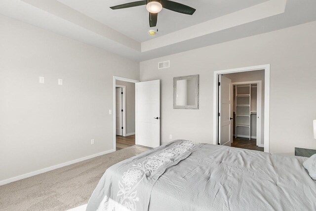 carpeted bedroom with a spacious closet, baseboards, a raised ceiling, ceiling fan, and visible vents