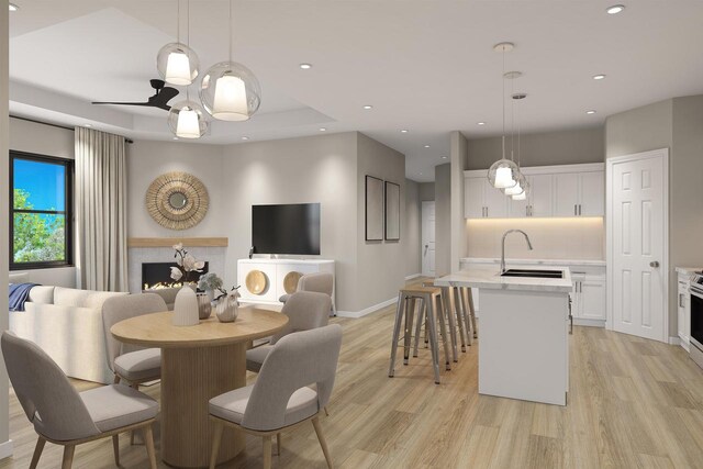 dining area featuring baseboards, recessed lighting, a lit fireplace, light wood-style floors, and a tray ceiling