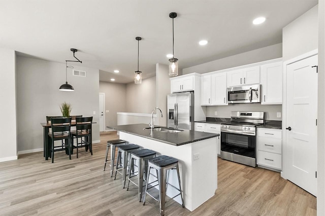kitchen with a sink, a kitchen breakfast bar, appliances with stainless steel finishes, visible vents, and dark countertops