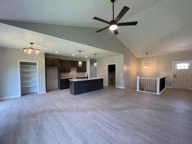 interior space featuring a center island, decorative light fixtures, vaulted ceiling, dark brown cabinets, and light wood-type flooring