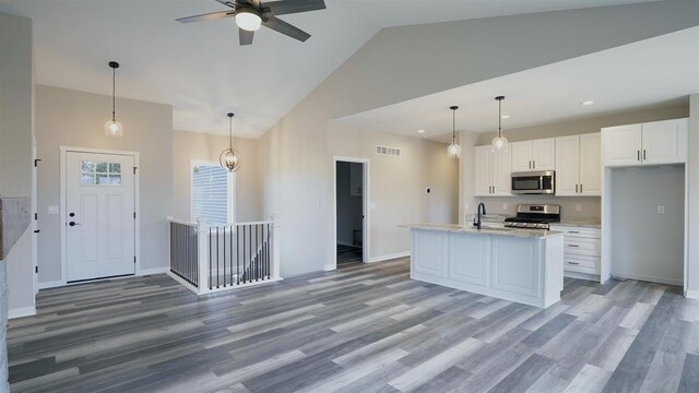 kitchen featuring appliances with stainless steel finishes, white cabinets, ceiling fan, decorative light fixtures, and a kitchen island with sink