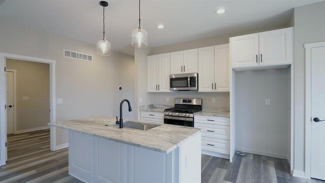 kitchen with appliances with stainless steel finishes, light stone counters, decorative light fixtures, a kitchen island with sink, and sink