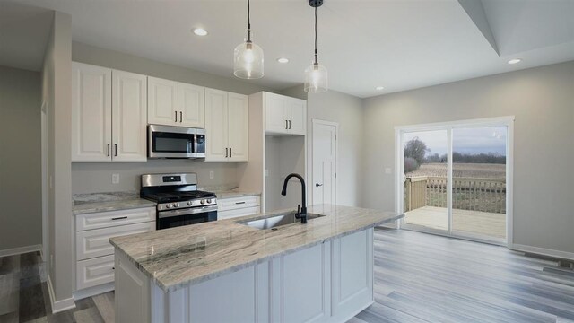 kitchen with sink, white cabinets, stainless steel appliances, a center island with sink, and light stone countertops