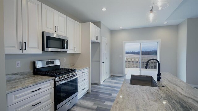 kitchen featuring appliances with stainless steel finishes, hanging light fixtures, white cabinetry, light stone counters, and sink