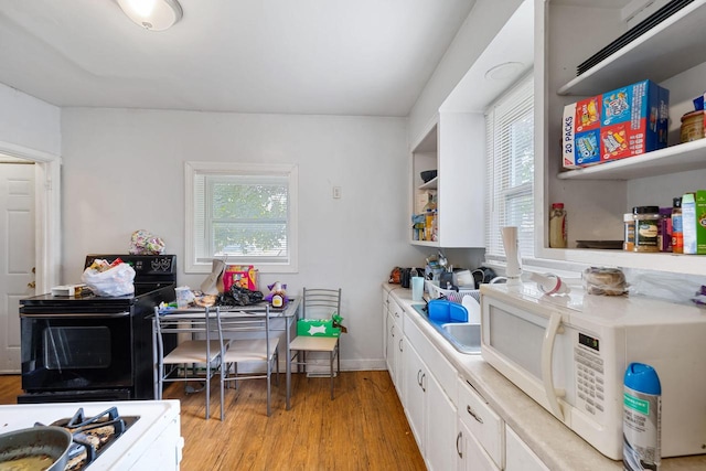 kitchen featuring light hardwood / wood-style flooring, white cabinets, plenty of natural light, and black range with electric stovetop